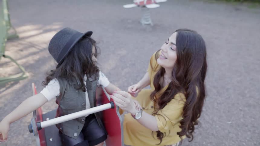 A mother crouching down to play with her child on spring rocker.
