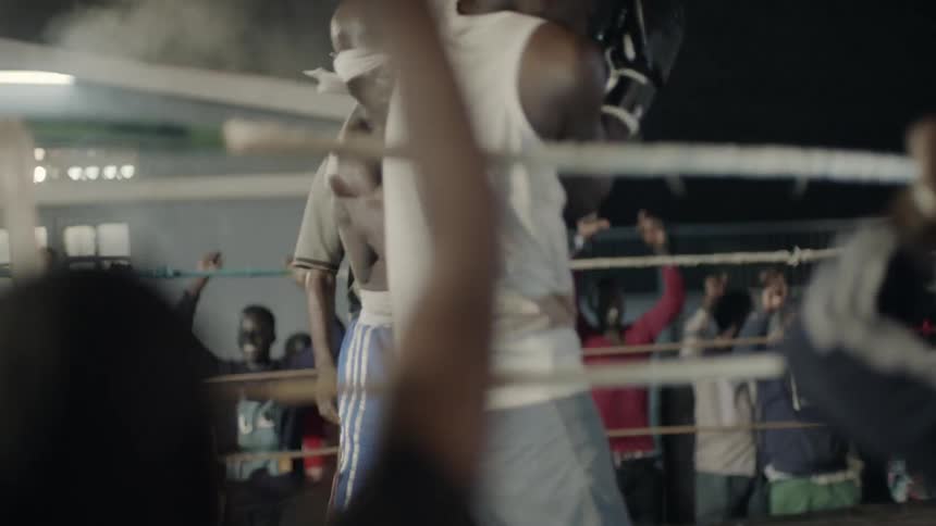 Two men box in a ring with an audience cheering behind them
