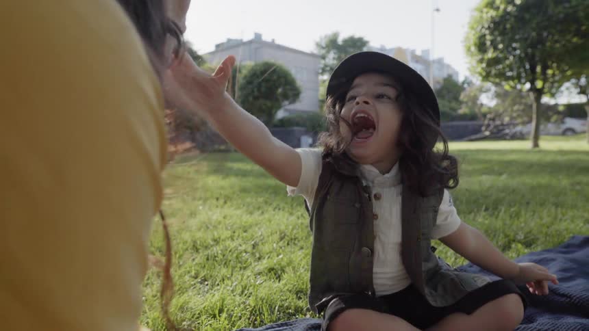 A happy young child wearing a black hat laughing outdoors during picnic.