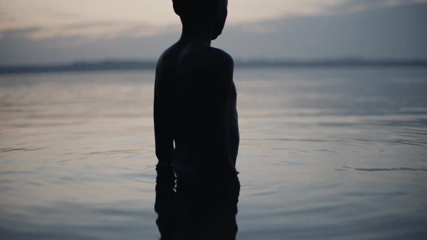 A boy stands in a lake at sunset