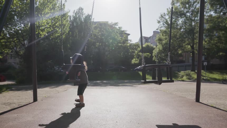 A young child standing near a swing set at park playground.