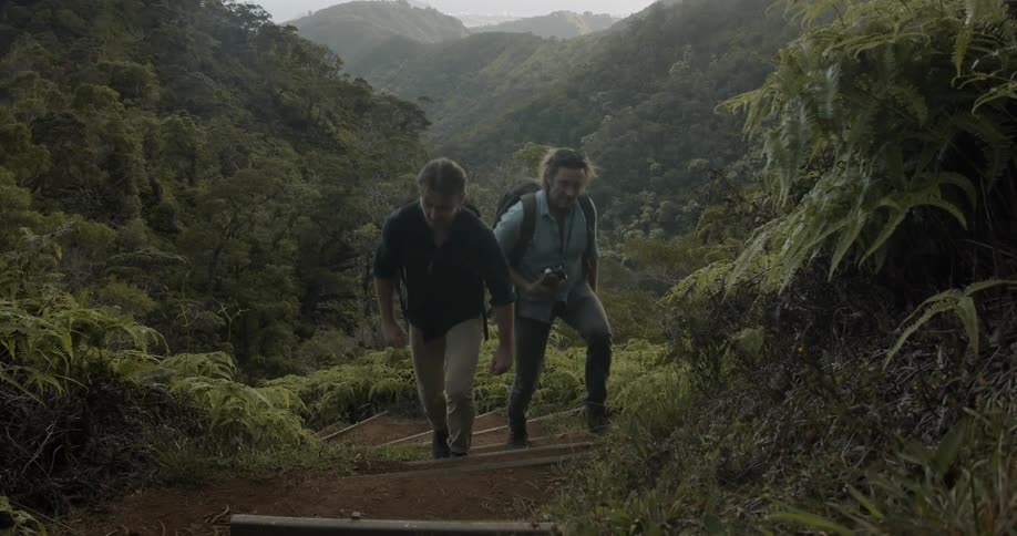 Two men hike up a path on tree covered hills
