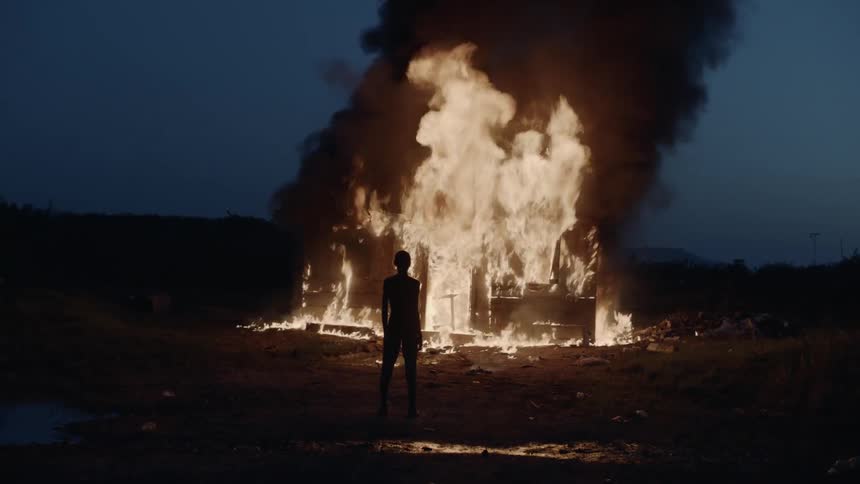 Thin person standing and watching a structure fire in a rural and dark area