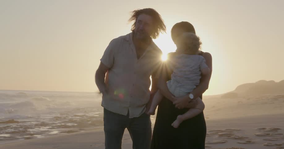 A young family stands on a beach at sunset