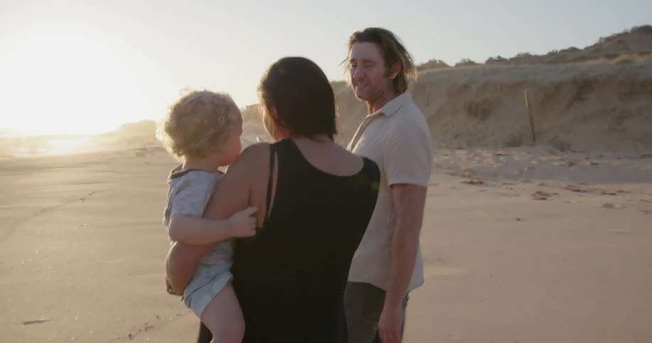 Man walks beside a woman carrying a child on the beach