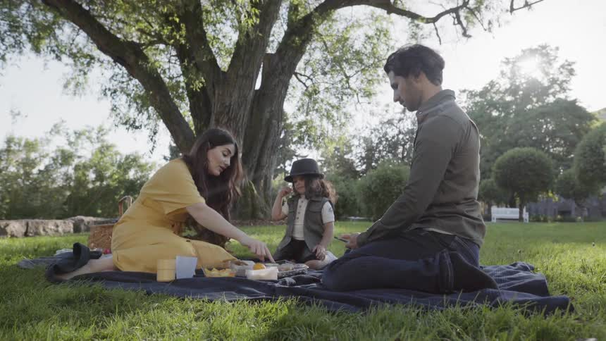 A young family sitting on blanket enjoying a sunny outdoor picnic.