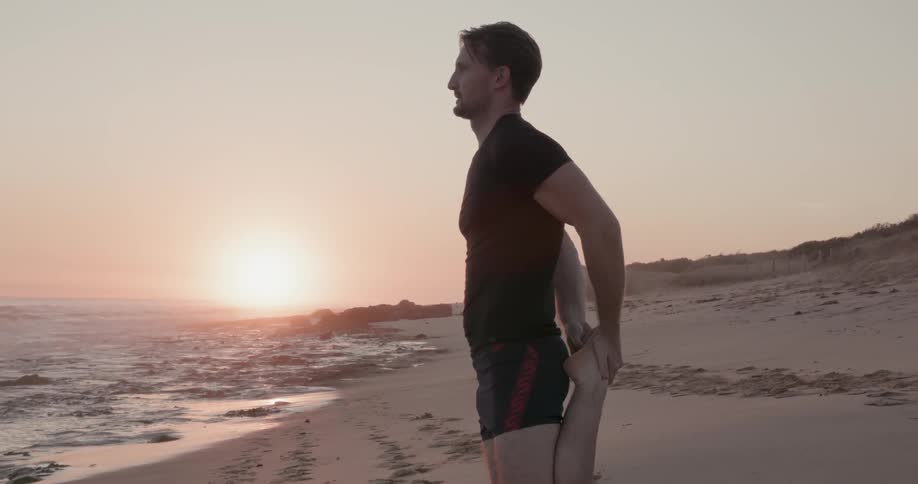 A man stretches on a beach at sunset
