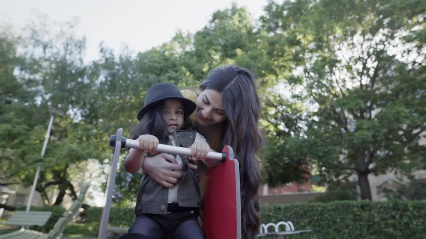 A loving mother hugging her young child from behind on playground rocker.