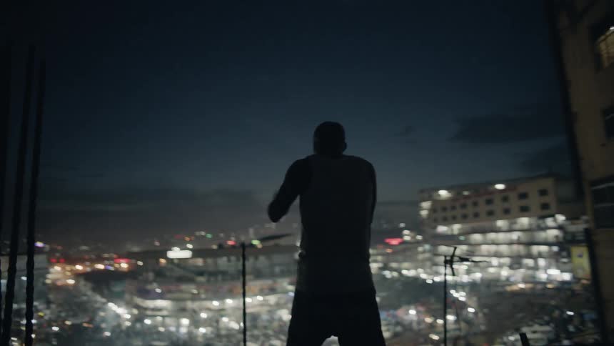 Man practices punching while standing on a rooftop overlooking a city at night