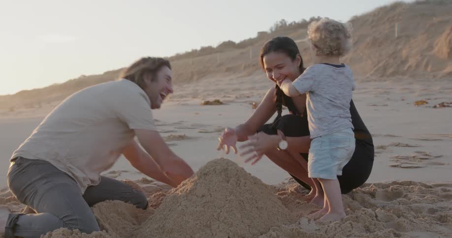A young family plays with sand on a beach at sunset