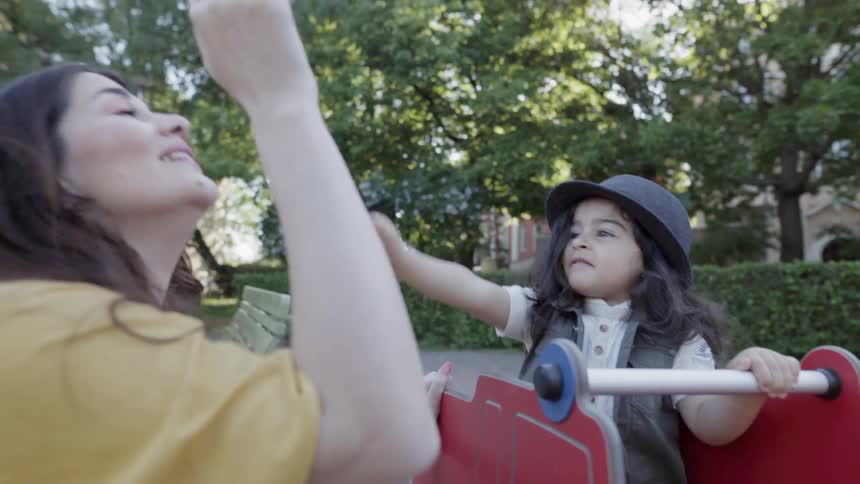 A young child playing high five game with mother at park playground.