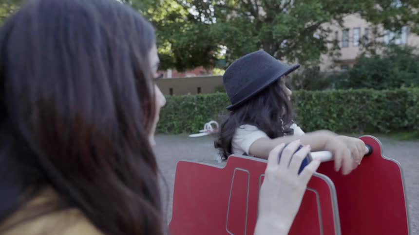 A loving mother watching her child play on a spring rocker playground.