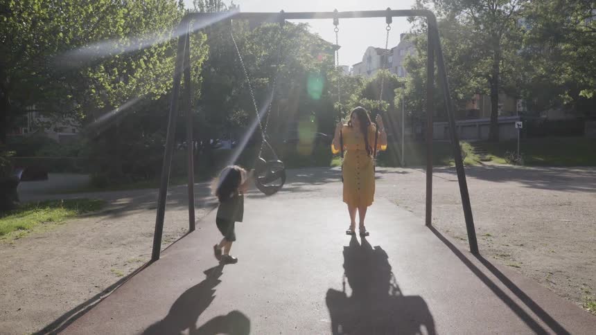 A happy mother and child swinging together on swings at park playground.