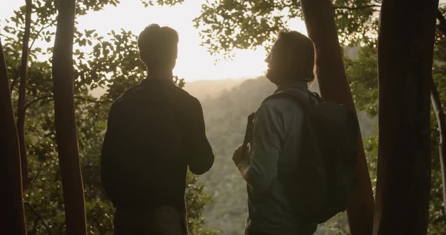 Two men hike in mountains at sunset