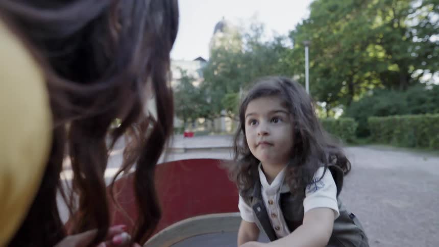A young child sitting on a playground rocker while talking to mother.
