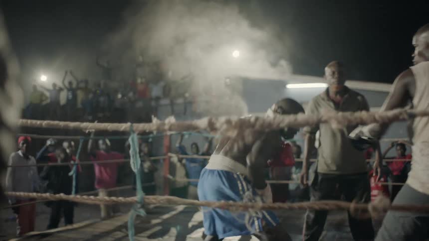 A crowd cheers for boxers at an outdoor boxing match