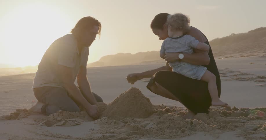 A young family builds a sandcastle on a beach at sunset
