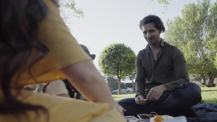 A man sitting cross-legged outdoors enjoying an open air family picnic.