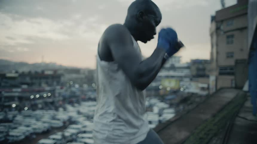 A boxer is shadow boxing on a rooftop at sunset