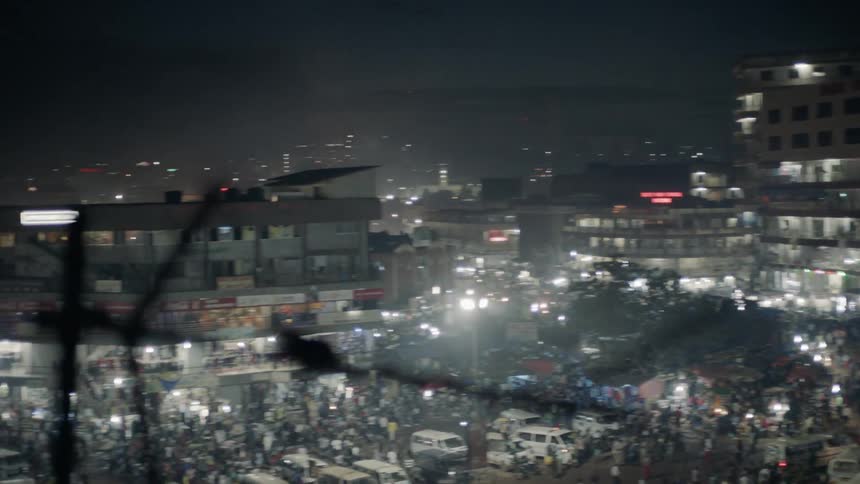 Lights shine from buildings in a city at night and many people walk the crowded streets