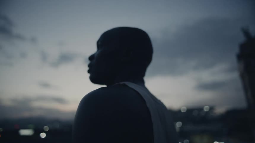 Man stands on a rooftop looking out at sunset