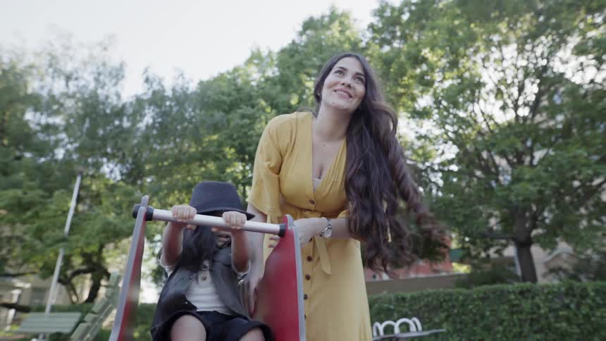 A mother standing behind her child and pushing a spring rocker playground.
