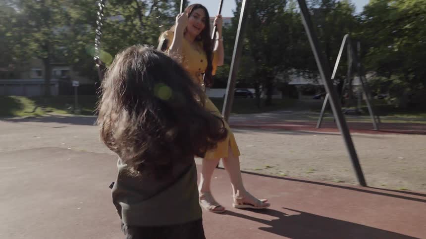 A young child running towards mother who is swinging at park playground.