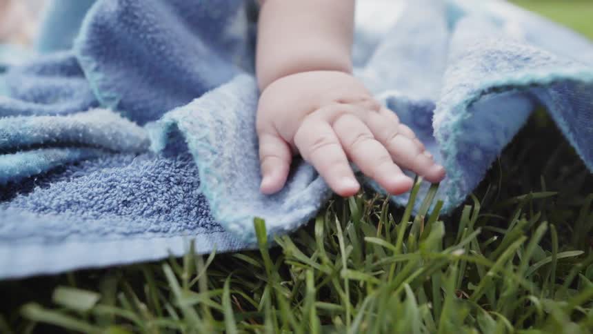 Gentle macro shot of a curious baby hand touching soft green grass outdoors.