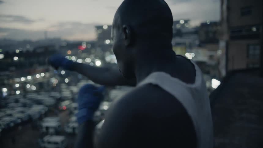 Man practices punching while standing on a rooftop overlooking a city