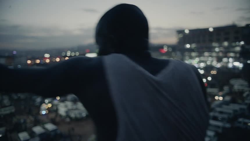 Man practices punching while standing on a rooftop overlooking a city on a cloudy evening