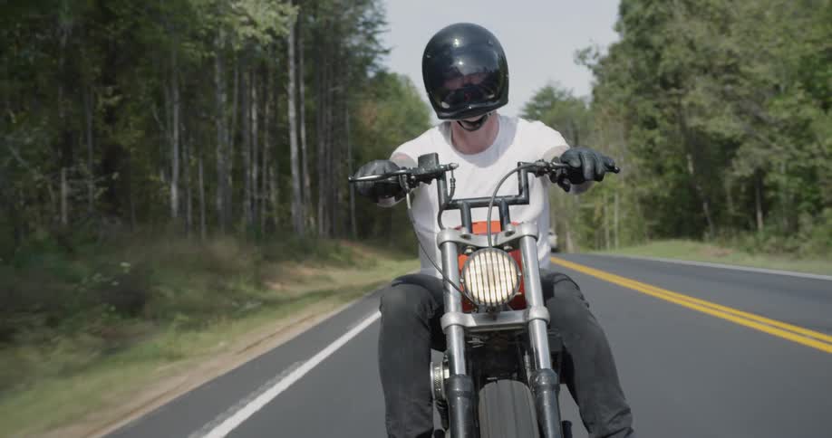 Man is riding motorcycle on sunny highway surrounded by trees