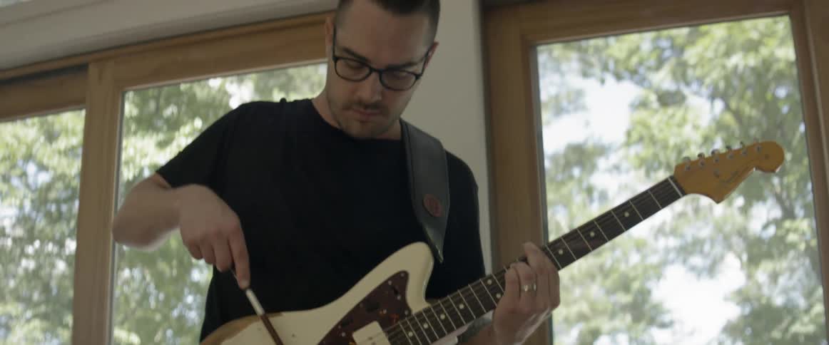 Man drags a violin bow across a guitar