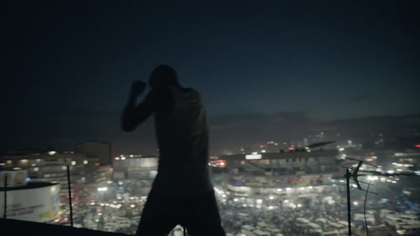 A boxer punches the air on a building rooftop