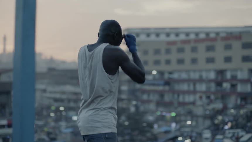 A boxer punches the air in a city at sunset