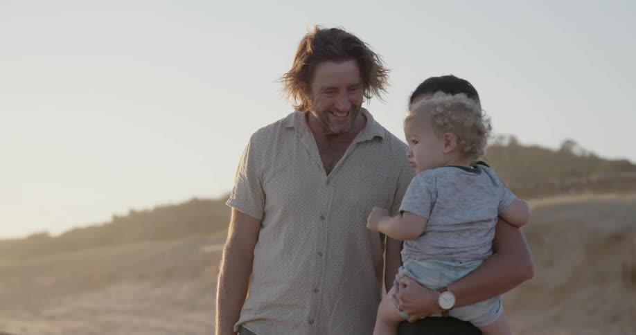 Man woman and child stand on the beach and the man smiles and points