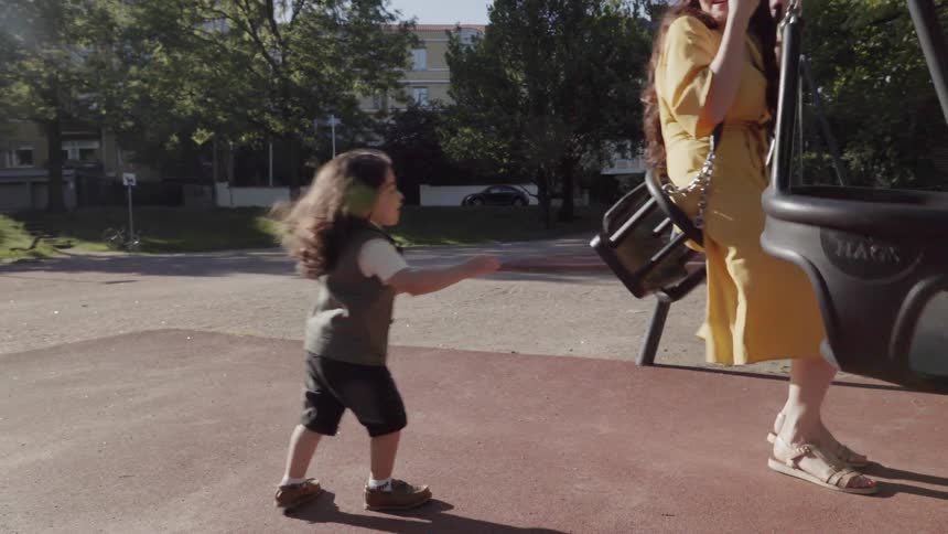 A young child pushing mother sitting on a swing at outdoor playground.