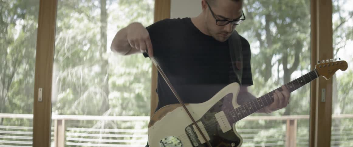 A man plays guitar with a bow