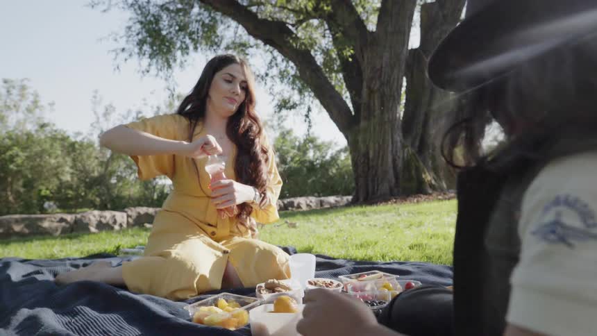 A young woman opening a bottle of juice during family outdoor picnic.