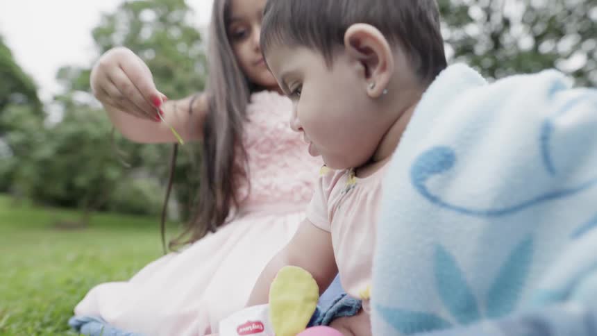 A girl and baby sit on a blanket on a lawn