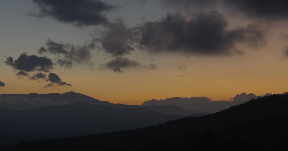 Clouds float over mountains at sunset