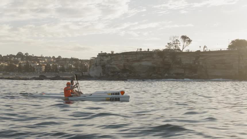 Two men kayak just off the coast at sunset