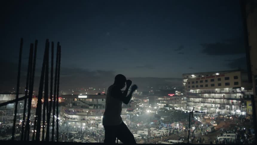 Man practices punching while standing on a rooftop overlooking a city at night
