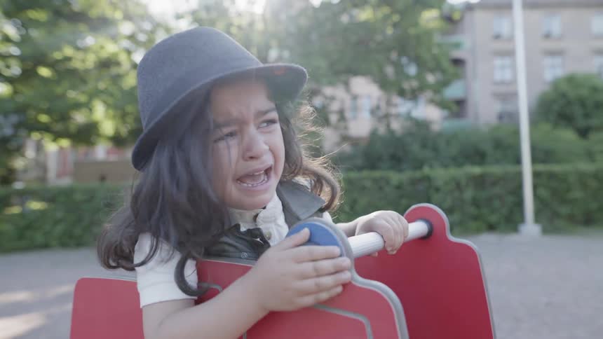 A young child crying while sitting on a spring rocker playground equipment.