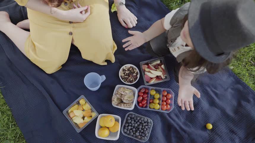 Fresh fruit containers spread on blanket during an outdoor family picnic.