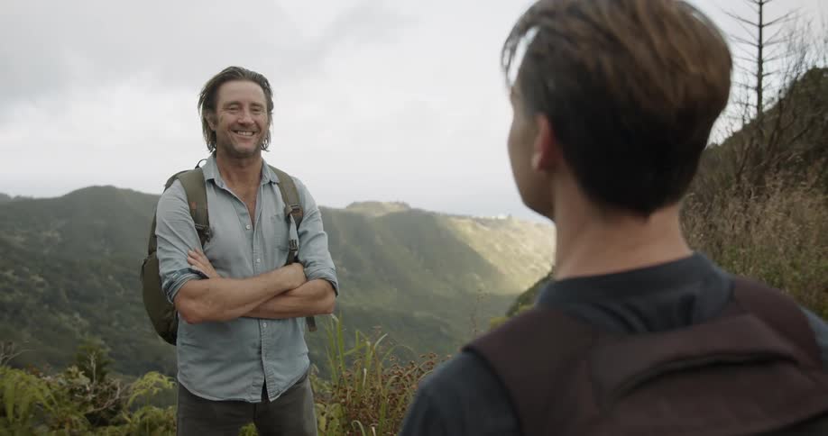 A man is taking another man's photo as they stand in a scenic area in daylight
