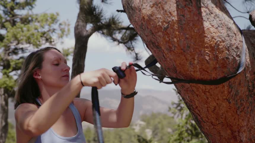 A woman ties a hammock to a tree