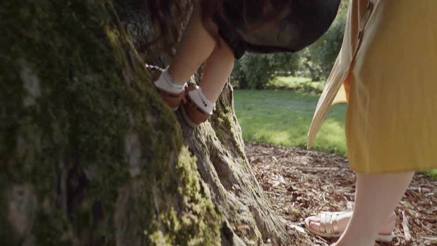 A caring mother helping her young child climb a large tree trunk.