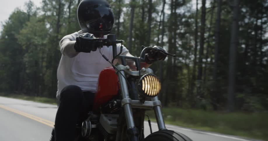 A man motorcycles on a tree-lined road