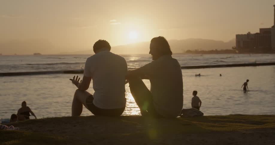 Two men talk on a beach at sunset