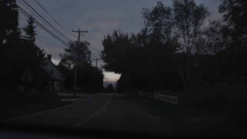 A vehicle travels down a rural road at dusk